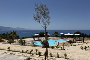 A pool area with lounge chairs and umbrellas, surrounded by small trees and a view of the sea. - Sea-view apartment with a pool (Telegrafo)