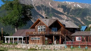 A wooden cabin with a balcony, a covered porch, and a mountain backdrop. - Carriage House at Roadhouse Lodge: romantic suite, fireplace & lake-view deck (Twin Lakes)