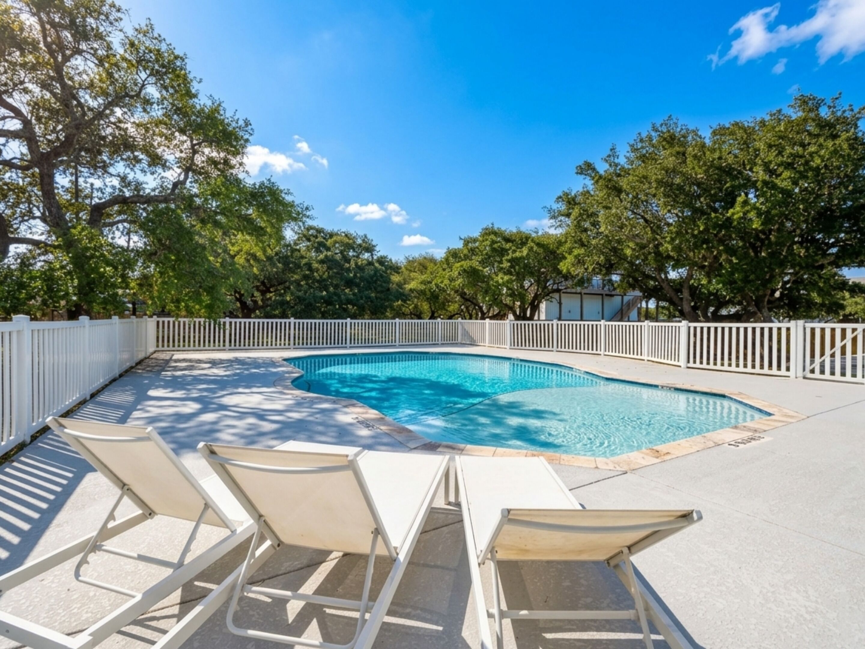 A swimming pool with white chairs and a white fence.