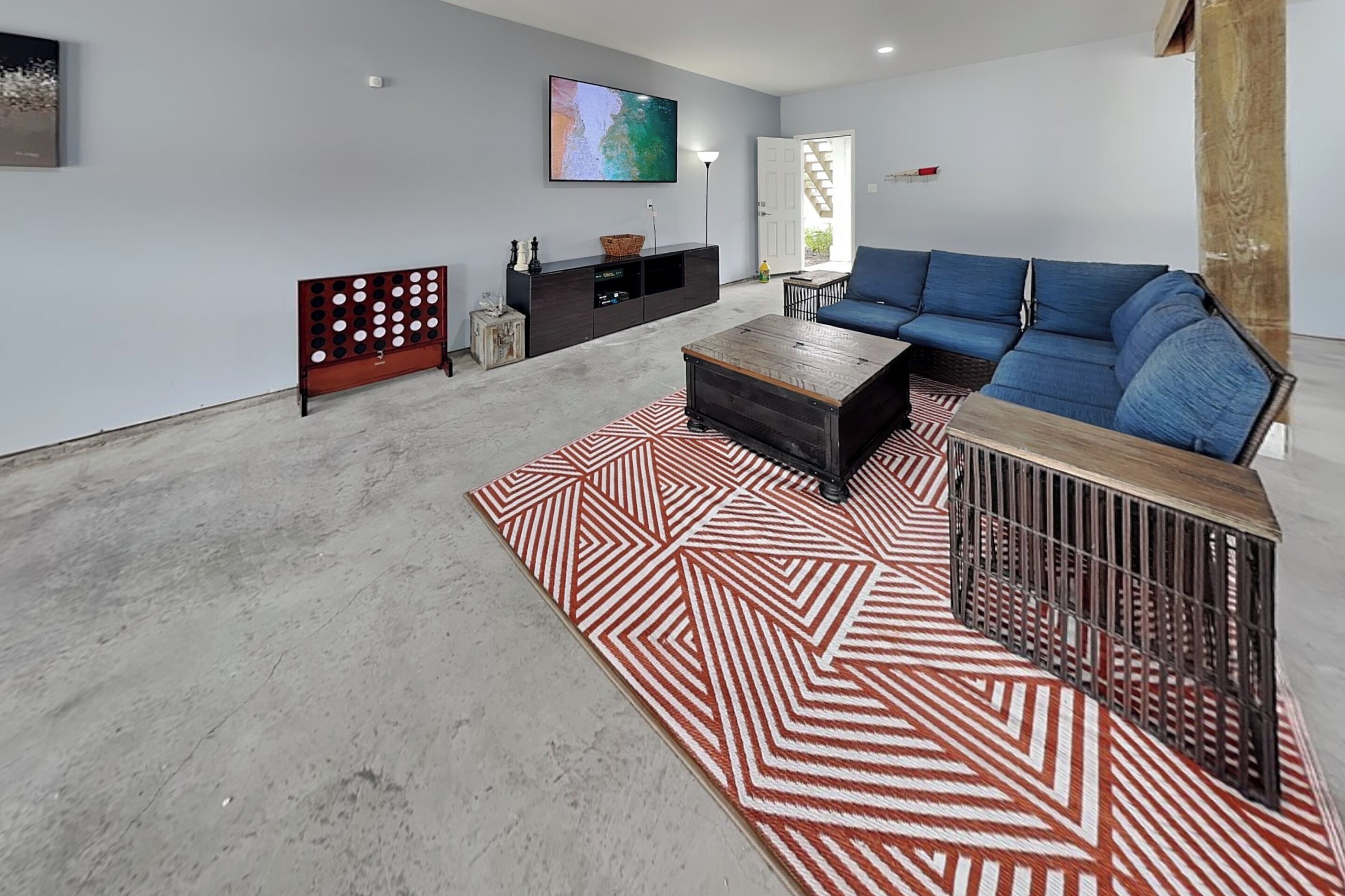 A living room with a blue sofa, a coffee table, a patterned rug, a TV on the wall, and a staircase.
