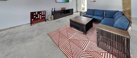 A living room with a blue sofa, a coffee table, a patterned rug, a TV on the wall, and a staircase.