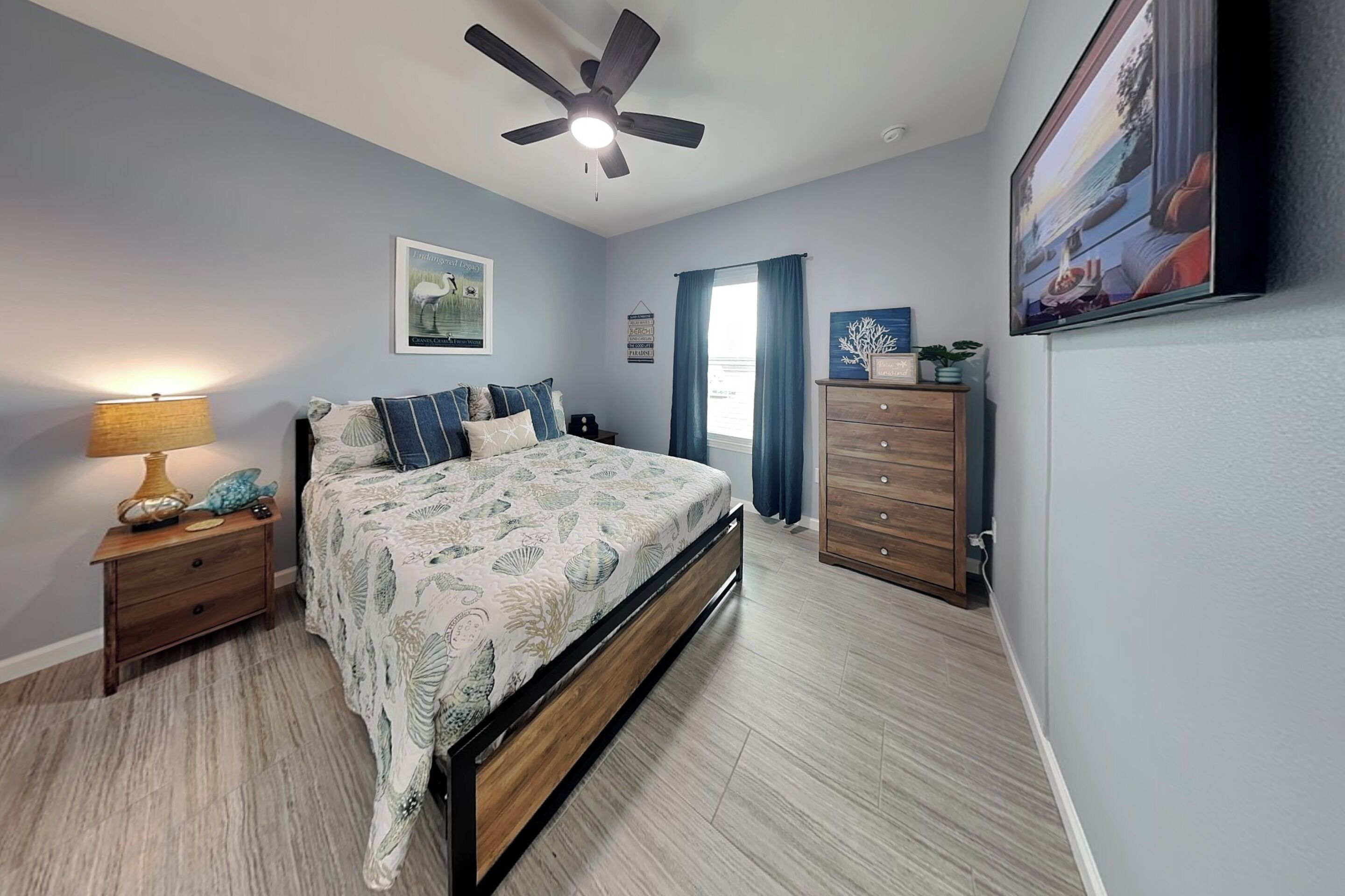 A bedroom with a bed, nightstands, a dresser, a ceiling fan, and a window with curtains.