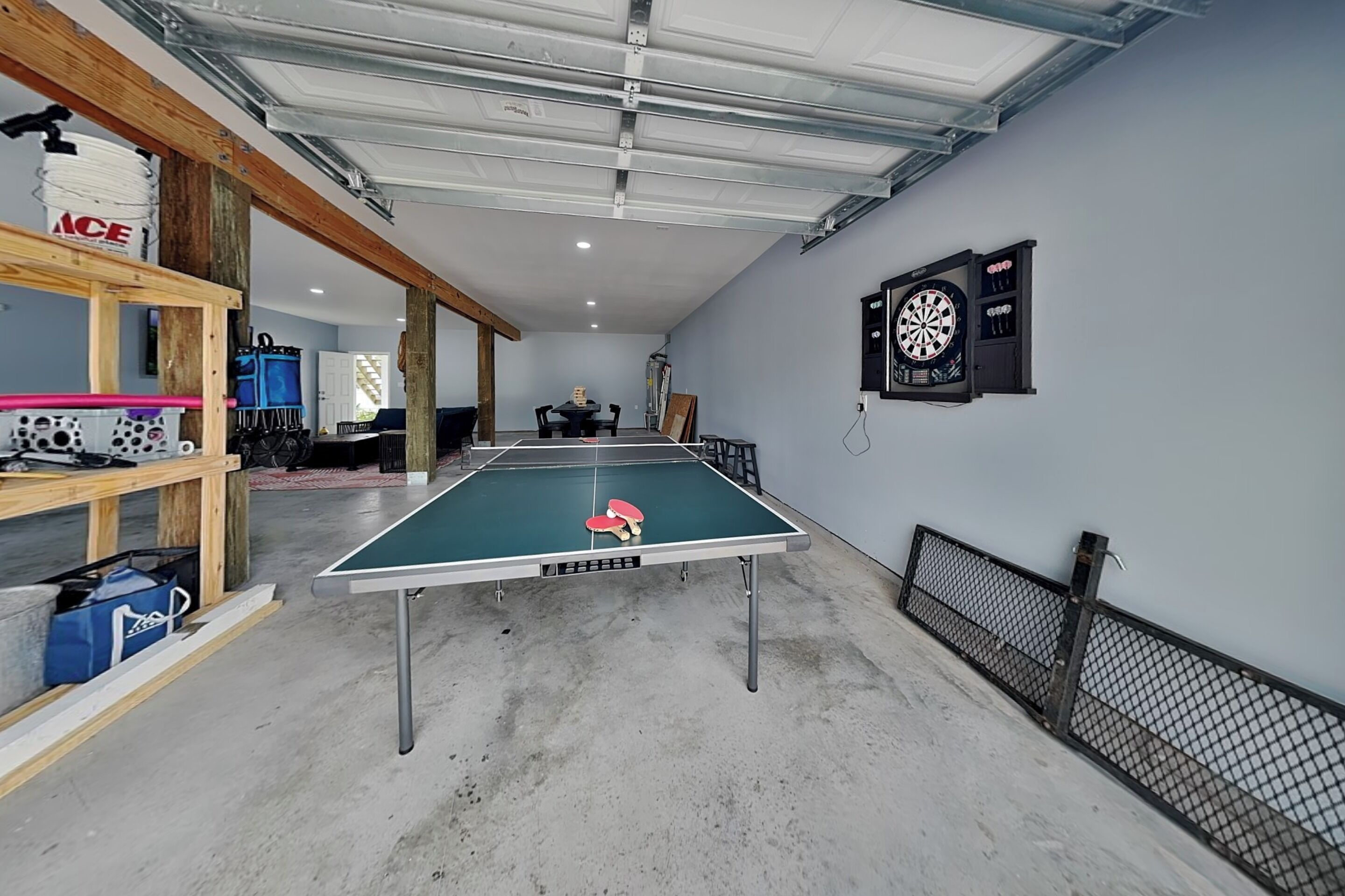 A ping pong table in a room with a dartboard and shelves with various items.