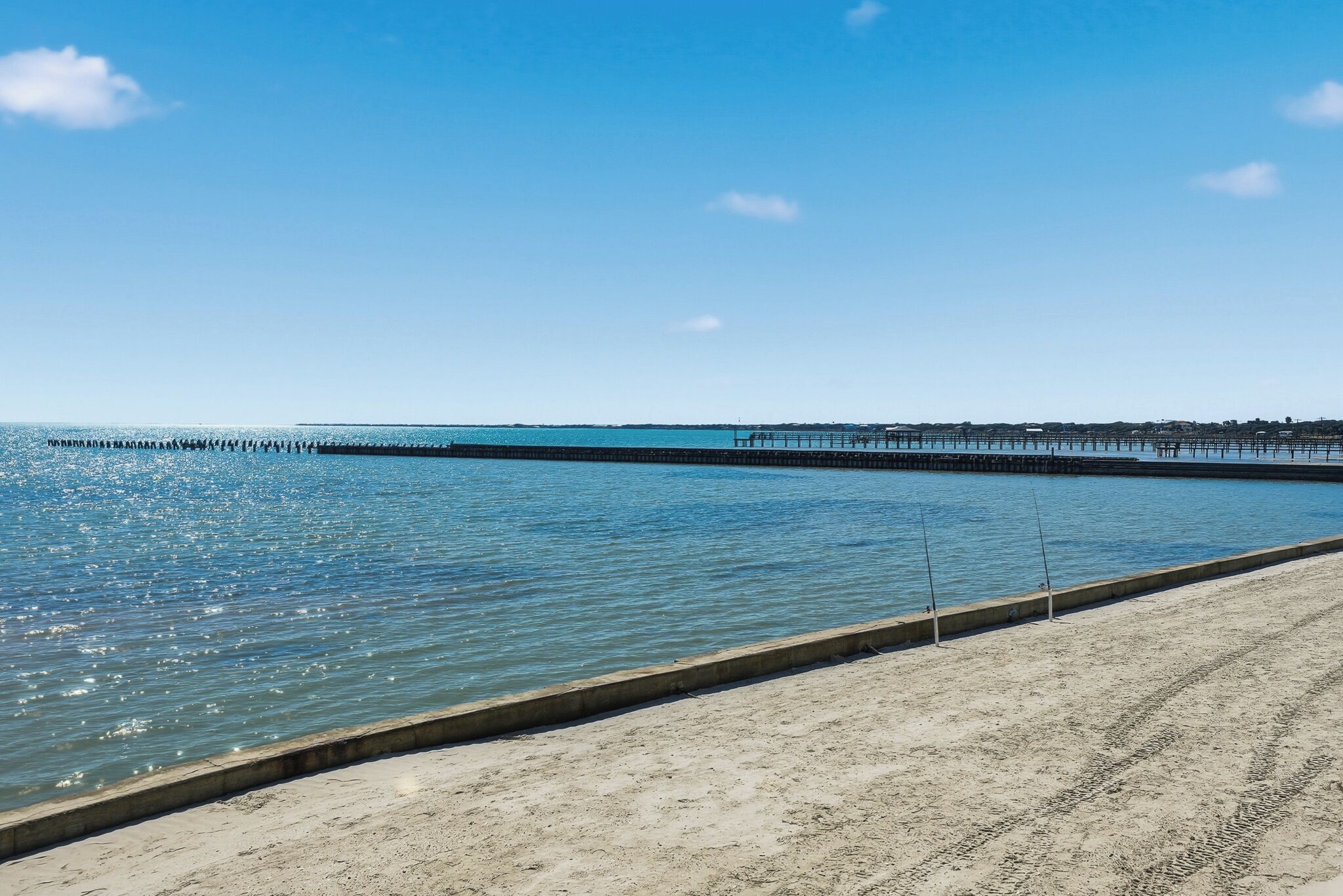 Una playa con un paseo de concreto y un muelle que se adentra en el agua.