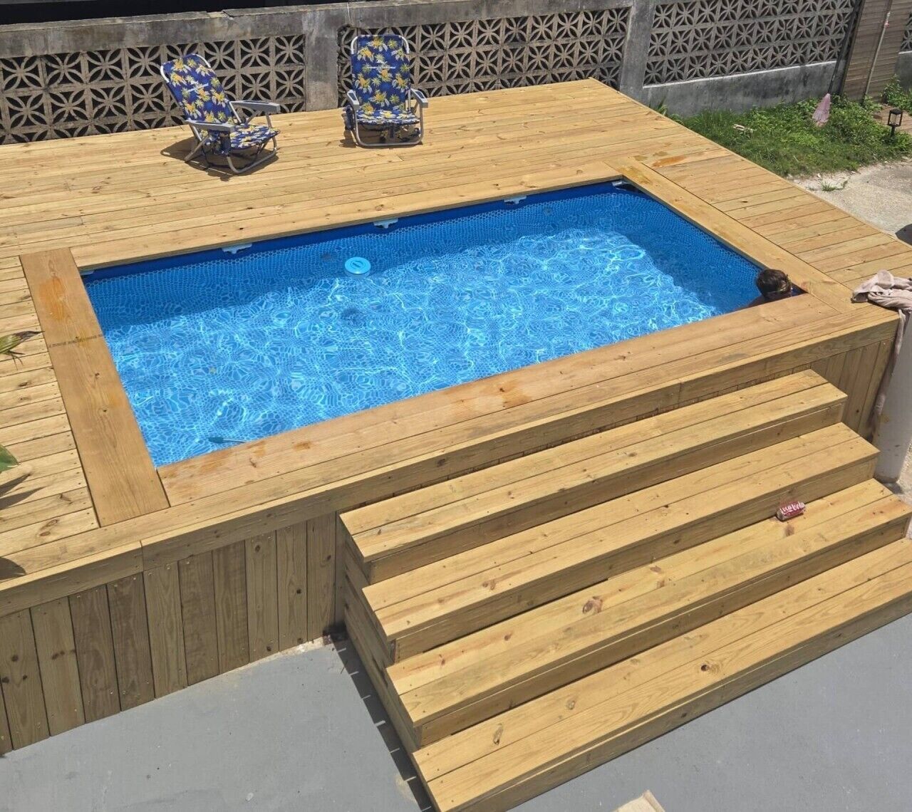 Una piscina rectangular con una cubierta de madera y escalones para entrar.
