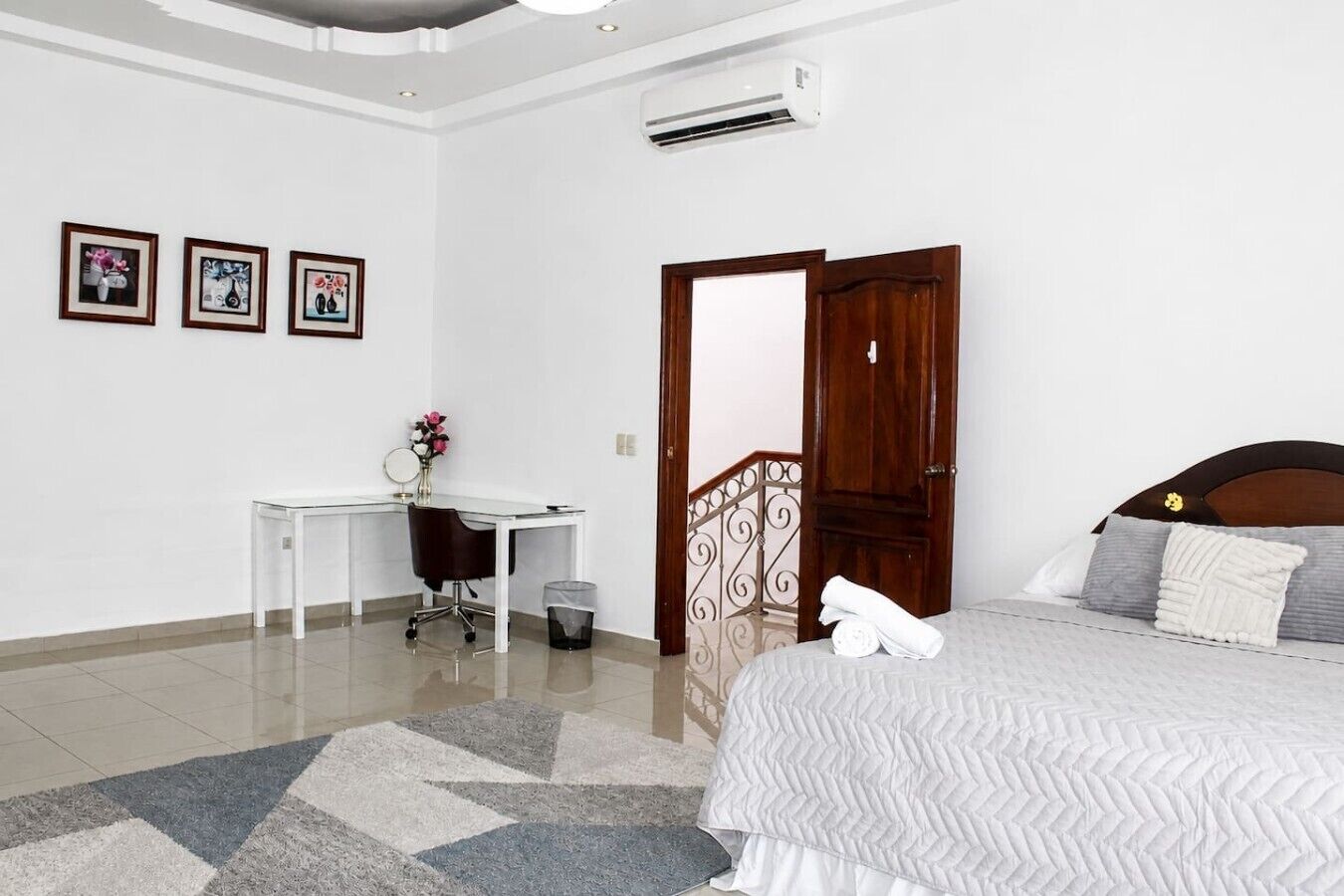 A hotel room with a bed, a desk, and a chair. There is a door with a decorative metal railing.