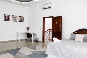 A hotel room with a bed, a desk, and a chair. There is a door with a decorative metal railing.