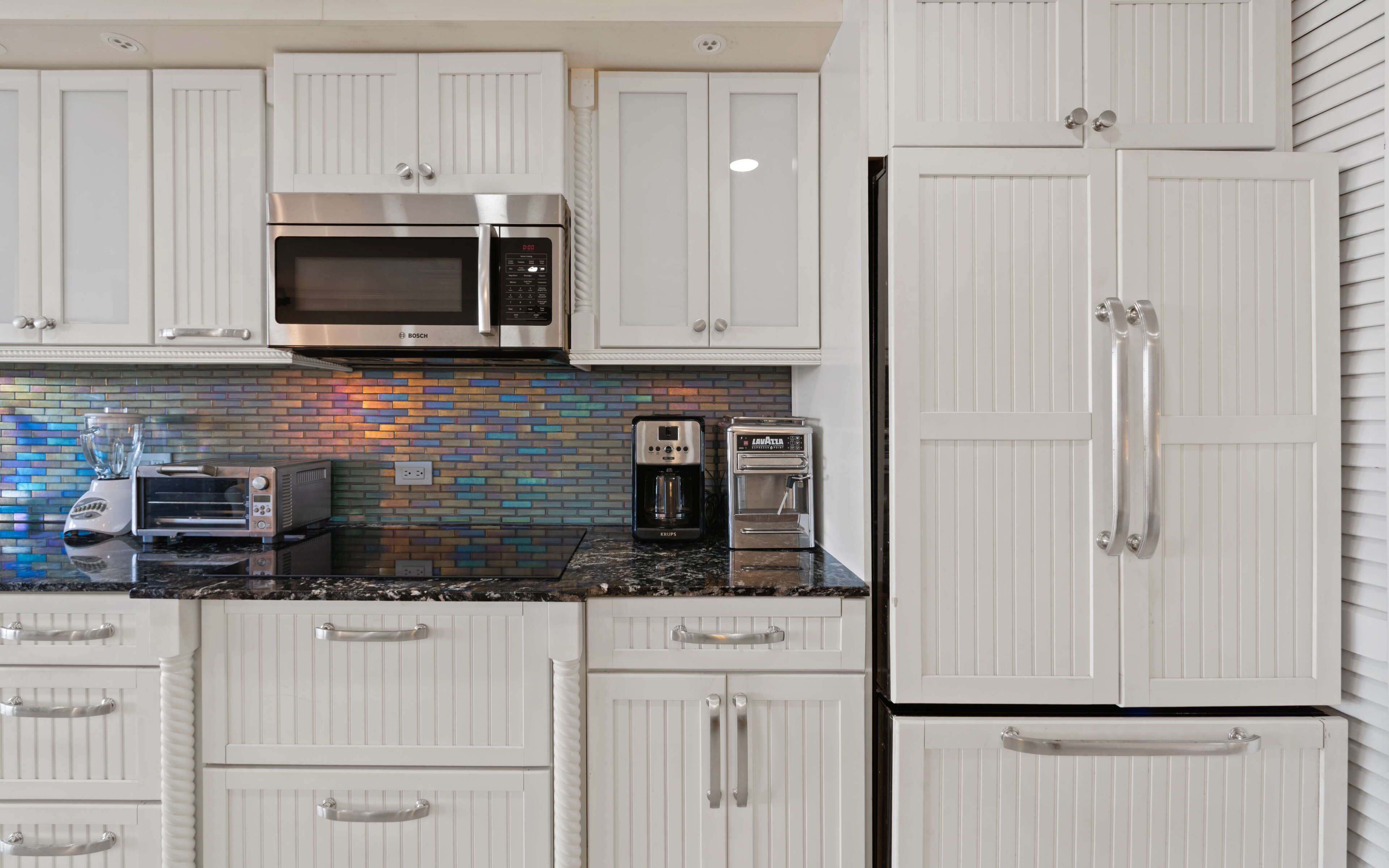 A kitchen with white cabinets, a Bosch microwave, a Krups coffee maker, and a toaster.