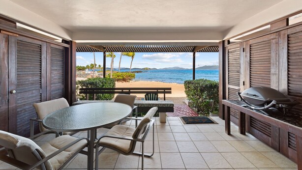 Uma área externa coberta com mesa, cadeiras, churrasqueira e vista para a praia e o oceano.