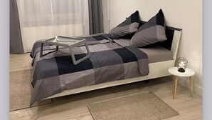 Une chambre à coucher moderne, avec un lit, une table de chevet, une lampe et une vue sur l’extérieur à travers des rideaux transparents.