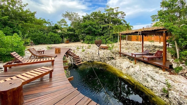 Una terraza de madera con sillones, un pequeño puente y una estructura con techo de paja.