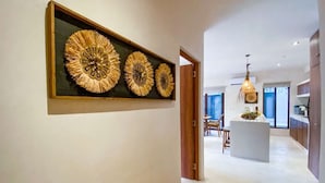 Un pasillo con un banco de madera, un reloj en la pared, y una zona de cocina con una isla central e iluminación colgante.
