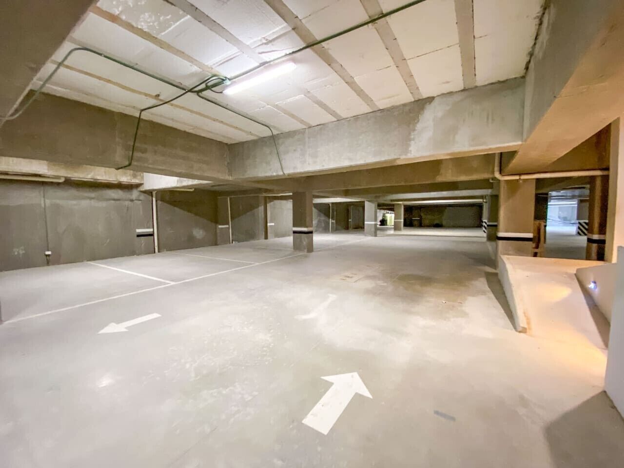 Un espace de stationnement intérieur doté de sols et de murs en béton, de places de stationnement délimitées et de flèches indiquant la direction.