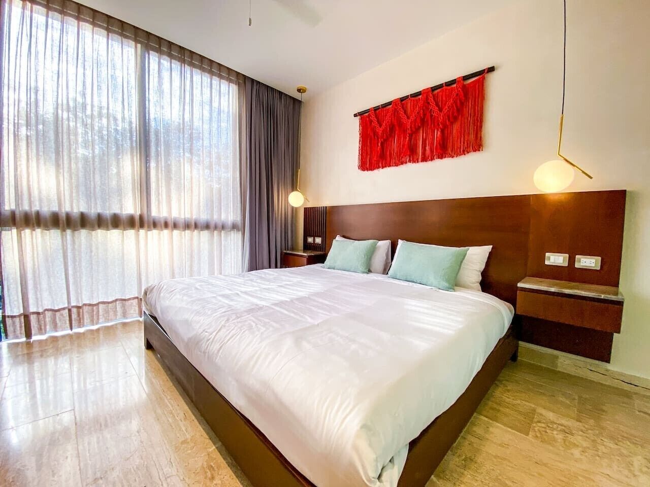 Un grand lit avec une tête de lit en bois, une table de chevet, une décoration murale rouge et une grande fenêtre avec des rideaux.