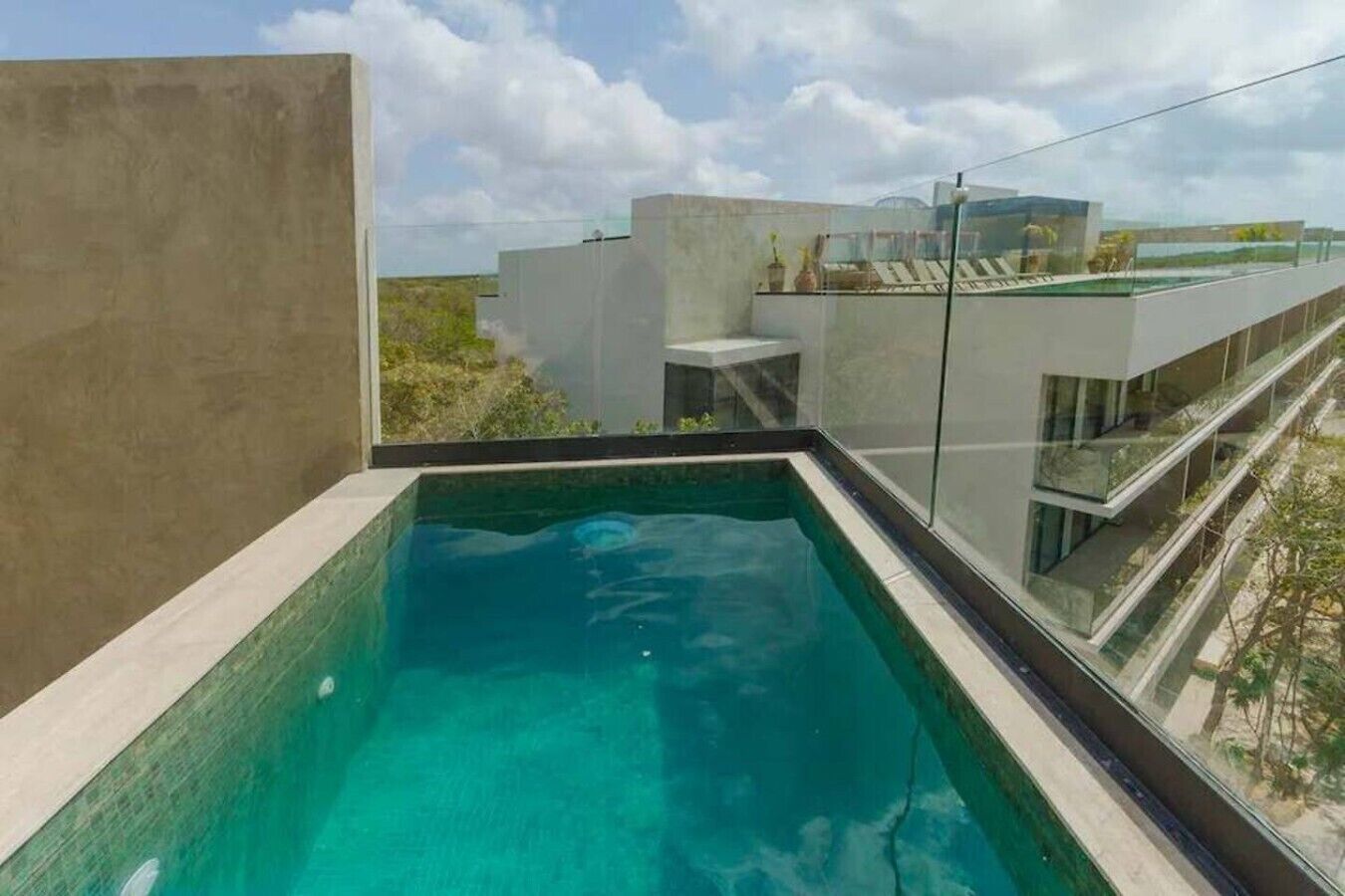 A modern rooftop pool with clear blue water, surrounded by glass walls and a concrete structure.