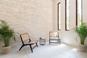 A room with a brick wall, two chairs, a small table, and potted plants. - Manor: Apt in Aldea Zama with pool (Tulum)