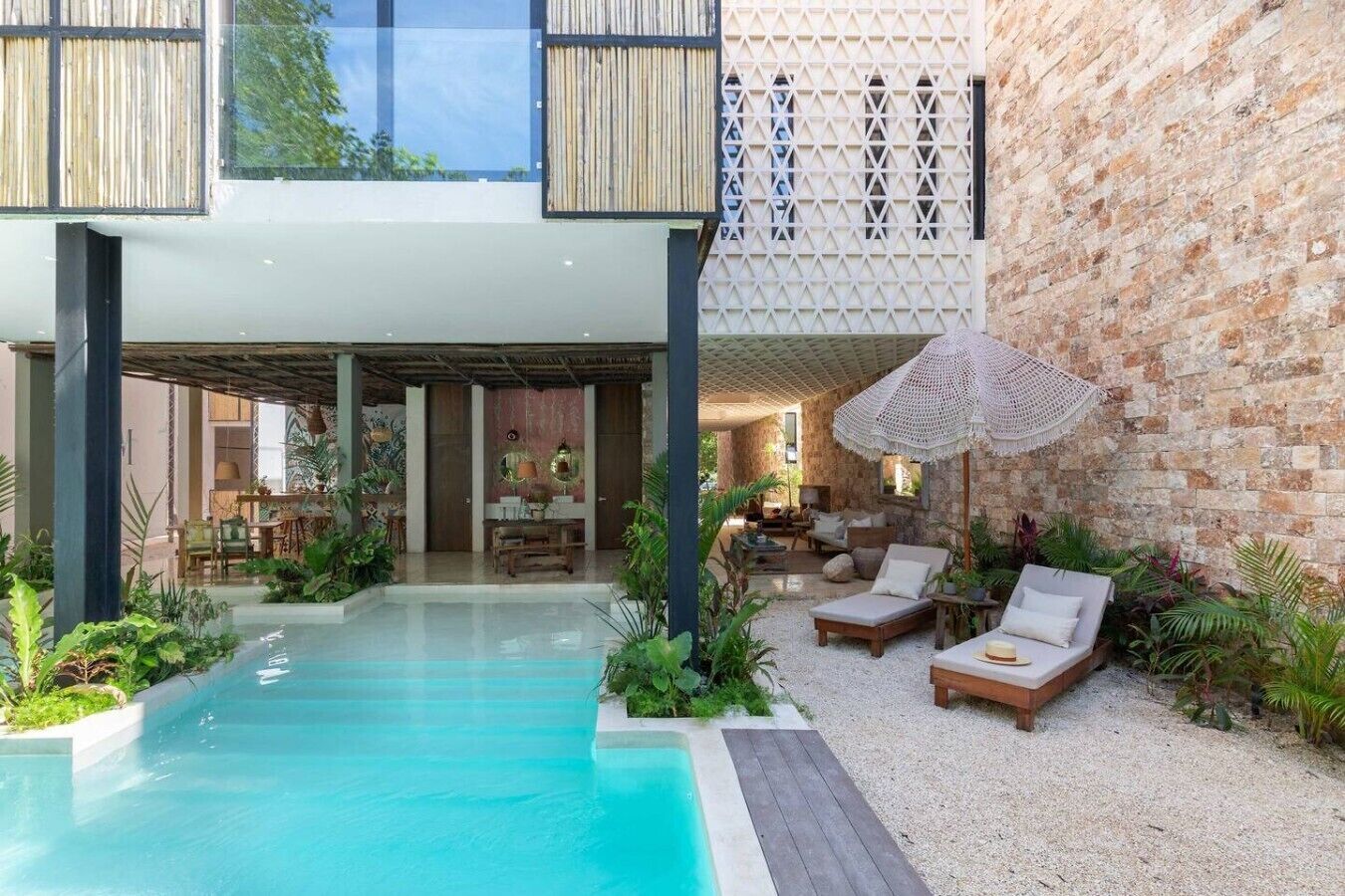A modern pool area with lounge chairs, a dining area, and a stone wall.