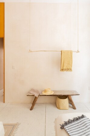 A minimalist room with a wooden bench, a hanging towel, and a straw basket. - Manor: Apt in Aldea Zama with pool (Tulum)