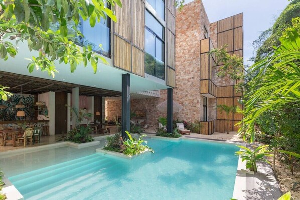 Un edificio moderno con piscina, area relax all'aperto e rigogliosa vegetazione.