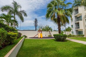 A playground with a slide and swings, surrounded by palm trees and a building with balconies. - Spacious Apt with 2BR and Pool in Cancún (Cancún)