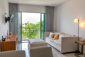 A modern living room with a sofa, a TV mounted on the wall, a wooden side table, and a balcony with greenery. - Spacious Apt with 2BR and Pool in Cancún (Cancún)