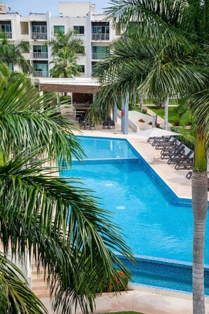 A swimming pool with lounge chairs, surrounded by palm trees and a modern building with balconies. - Spacious Apt with 2BR and Pool in Cancún (Cancún)