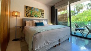 A bedroom with a bed, a floor lamp, a painting, and a view of greenery through a sliding door. - Sabor a Miel: Two seaside apartments (Playa del Carmen)