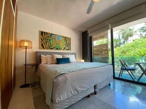 Ein Schlafzimmer mit einem Bett, einer Stehlampe, einem Gemälde und Blick auf Grün durch eine Schiebetür.