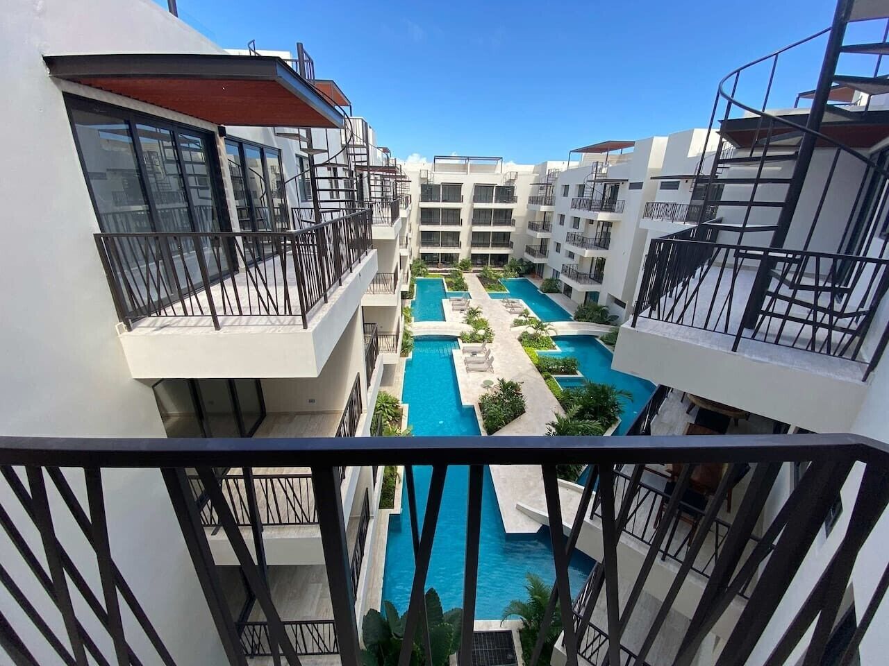A multi-story hotel with balconies, a central swimming pool, and a clear sky.