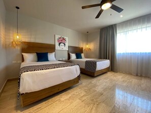 Ein Hotelzimmer mit zwei Betten, einem Deckenventilator, einem Gemälde und einem großen Fenster mit Vorhängen.