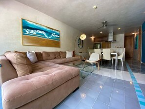 Ein modernes Wohnzimmer mit einer Eckcouch, einem Essbereich mit Glastisch und einer Küche im Hintergrund.