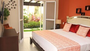 A bedroom with a bed, a nightstand, a lamp, a TV, and a sliding door leading to a garden. - Ground floor Condo, Steps from Coco Beach & 5th Av (Playa del Carmen)