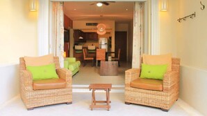 A room with two wicker sofas with cushions, a small wooden table, and a view into a dining area with chairs and a table. - Ground floor Condo, Steps from Coco Beach & 5th Av (Playa del Carmen)
