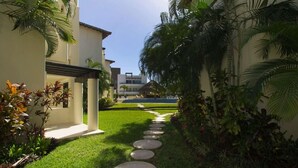 A pathway with stepping stones leading to a building with a white facade and a covered area. - Ground floor Condo, Steps from Coco Beach & 5th Av (Playa del Carmen)