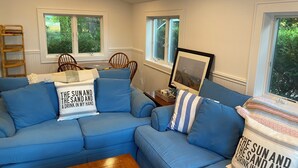 A living room with a blue sectional sofa, a wooden coffee table, and a framed picture on the wall. - Cozy 2-bedroom waterfront cottage with central AC, patio, BBQ, Private beach (Hampton Bays)