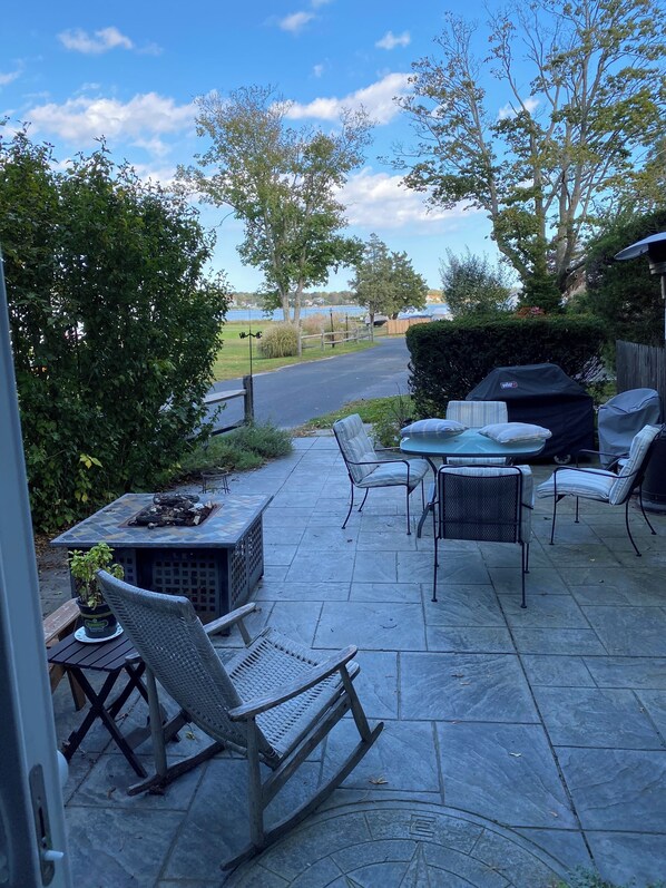 Un patio con mobiliario exterior, una parrilla y vistas a una carretera y árboles.