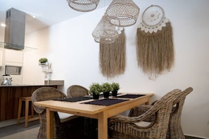 A dining area with wicker chairs, a wooden table, and wall decorations including a dreamcatcher and hanging tassels. - Lunada: Bright Stay with Rooftop Amenities (Playa del Carmen)