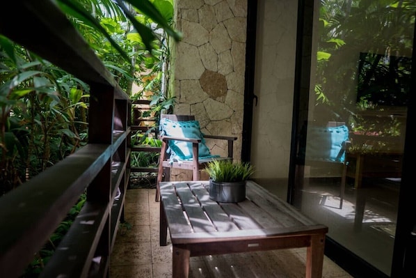 A sunlit patio with wooden furniture, a stone wall, and lush greenery. - Lunada: Bright Stay with Rooftop Amenities (Playa del Carmen)