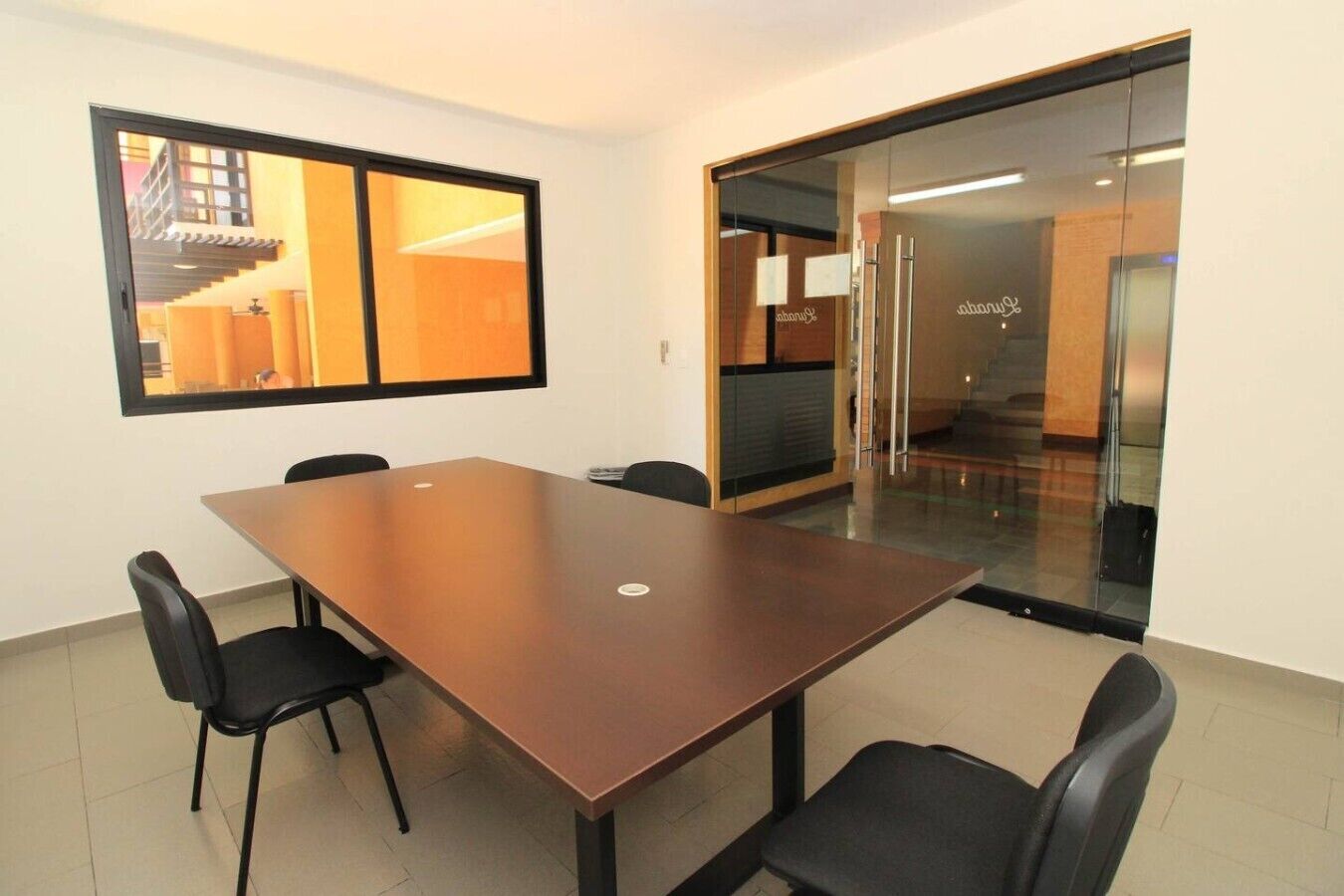 A conference room with a long table, four chairs, a large window, and a glass door leading to a staircase.