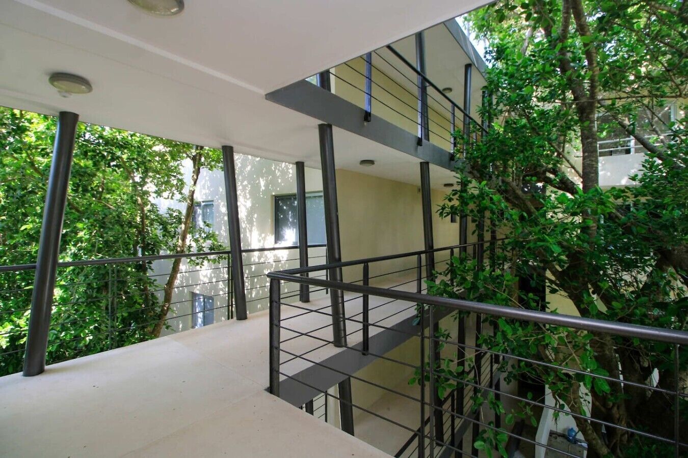 A multi-level outdoor staircase with metal railings and glass balustrades, surrounded by greenery and trees.