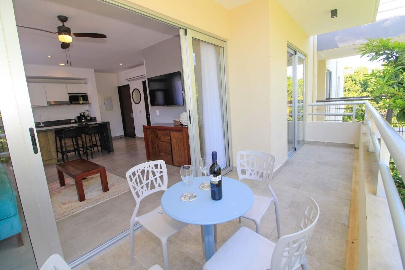 A balcony with a table and chairs, a bottle of wine, and a TV in the background.