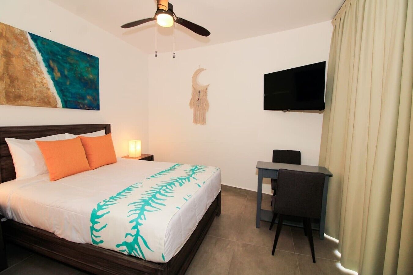 Ein Hotelzimmer mit Bett, Schreibtisch, Fernseher und Deckenventilator.