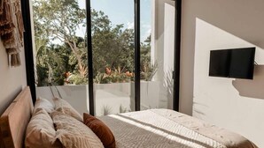 Une chambre moderne avec une grande fenêtre, un lit recouvert d’une couverture à motifs et un téléviseur fixé au mur.