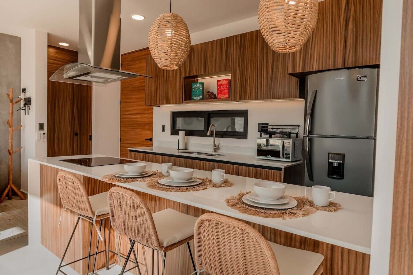 Una cocina moderna con una isla central, electrodomésticos integrados y sillas de mimbre.
