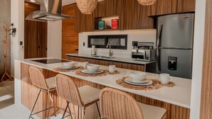 Une cuisine moderne dotée d’un îlot central, d’appareils électroménagers intégrés et de chaises en osier.