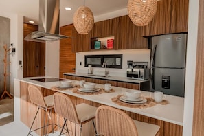 Une cuisine moderne dotée d’un îlot central, d’appareils électroménagers intégrés et de chaises en osier.