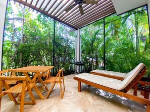Eine überdachte Terrasse mit Holzmöbeln, darunter ein Tisch, Stühle und zwei Liegestühle.