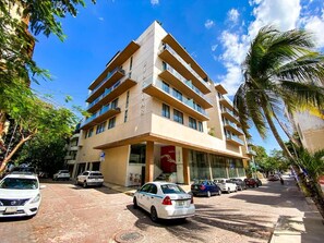 A multi-story hotel with a central entrance, a parking area, and a clear blue sky. - Joy: Apt with rooftop and panoramic views (Playa del Carmen)