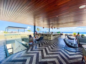 A modern outdoor lounge area with a glass balustrade, seating, and a view of the beach. - Joy: Apt with rooftop and panoramic views (Playa del Carmen)