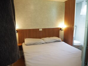 Ein Schlafzimmer mit Bett, Holz-Kopfteil, Nachttischlampe und Blick ins Bad.